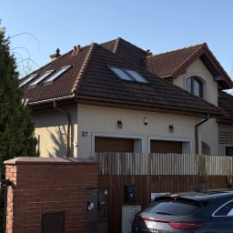 GreenCert Wojciech Mroczkowski - Dwukondygnacyjny dom z brązowym dachem i oknami dachowymi, widoczny zza ogrodzenia. Na elewacji numer 37 i lampy. Częściowo widoczny samochód.