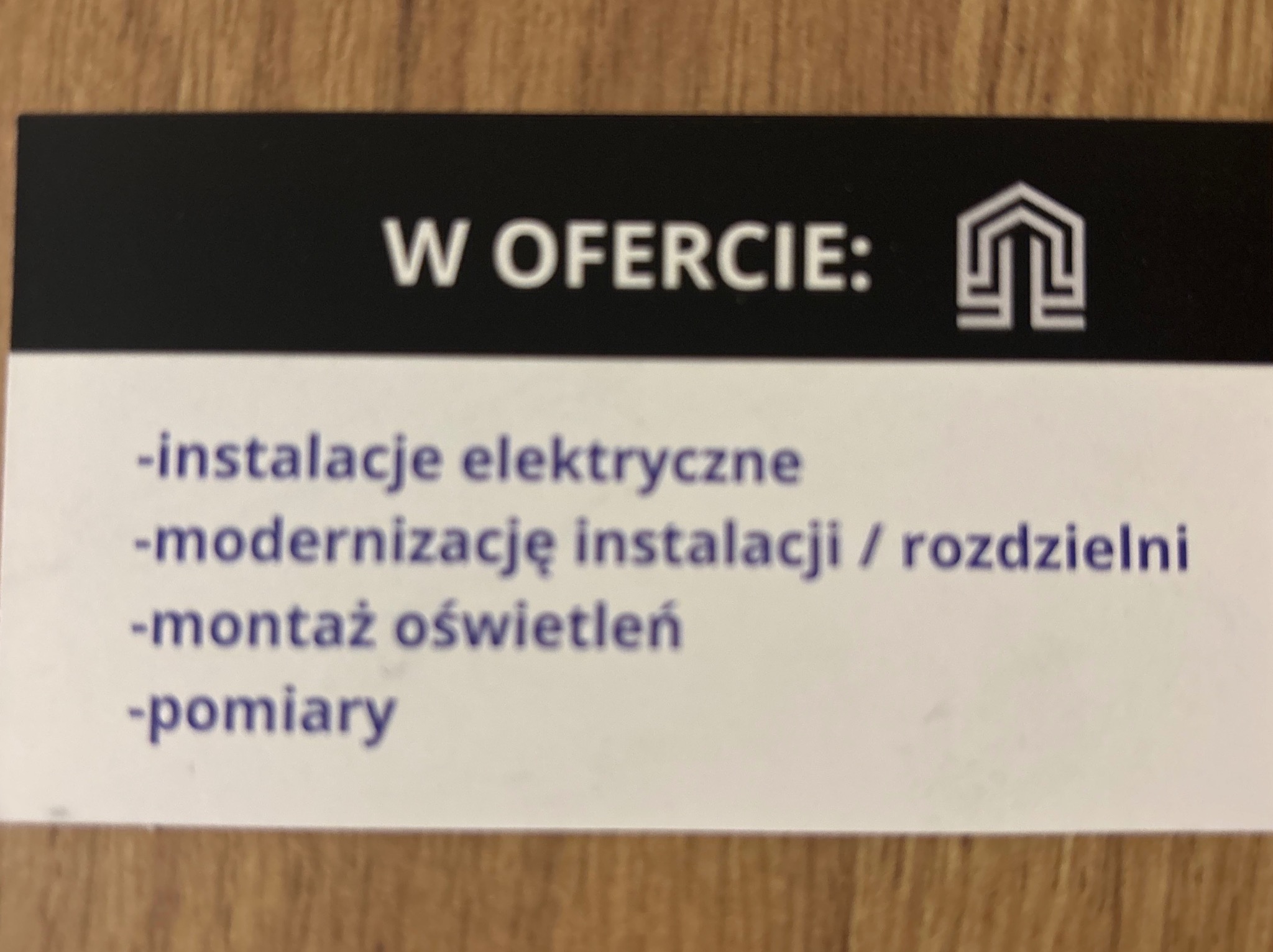 Wizytówka elektryka z ofertą: instalacje elektryczne, modernizacja instalacji/rozdzielni, montaż oświetleń, pomiary. Logo firmy w górnym rogu.