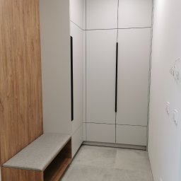 IDEA Damian Dyoniziak - Nowoczesna szafa wnękowa z siedziskiem w przedpokoju. Białe fronty szafy z długimi, czarnymi uchwytami. Drewniane wykończenie siedziska i panelu ściennego.