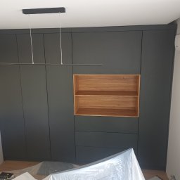 IDEA Damian Dyoniziak - Ciemnoszara szafa wnękowa z drewnianą wstawką i oświetleniem LED, klimatyzator na ścianie. Widoczne zabezpieczenia podłogi folią malarską.