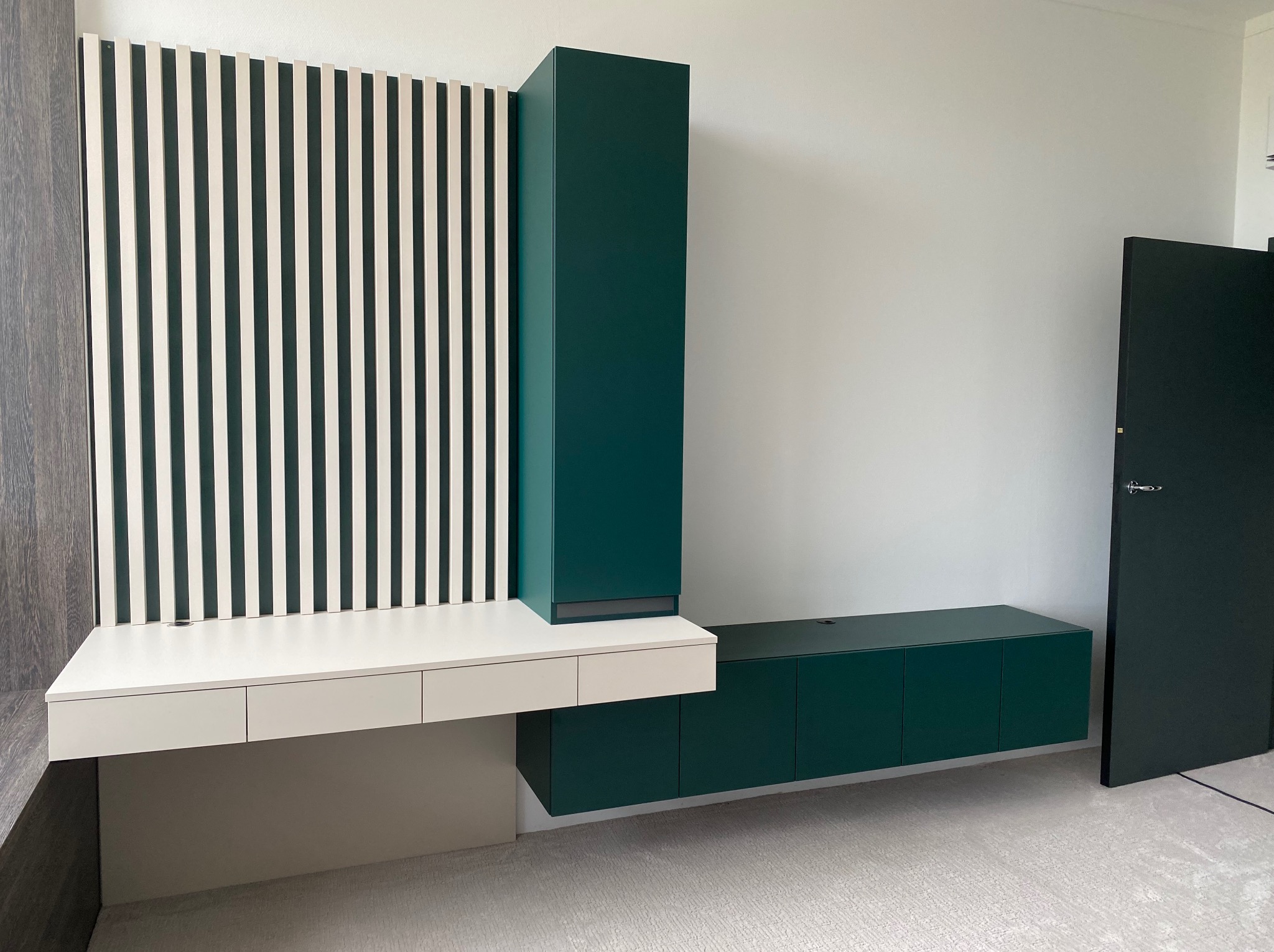 Nowoczesny zestaw mebli: biurko z szufladami, pionowa szafka i szafka RTV w odcieniach bieli i butelkowej zieleni, z dekoracyjnym panelem lamelowym.