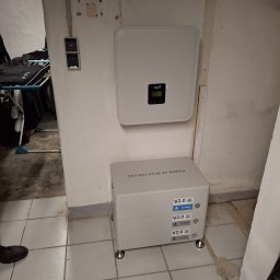 ENOX Robert Koprek - Zamontowany magazyn energii Fox ESS V2.0 z falownikiem na ścianie w pomieszczeniu. Widoczne trzy moduły bateryjne i falownik. Tło to ściana z widocznymi śladami po instalacji.