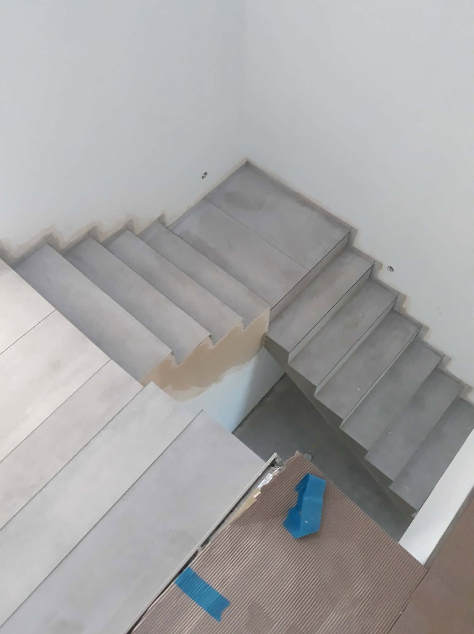 Układanie płytek na schodach w Łodzi. Widoczne płytki w odcieniach szarości, narzędzia glazurnicze i fragment wykończonej powierzchni. Prace wykończeniowe w trakcie.