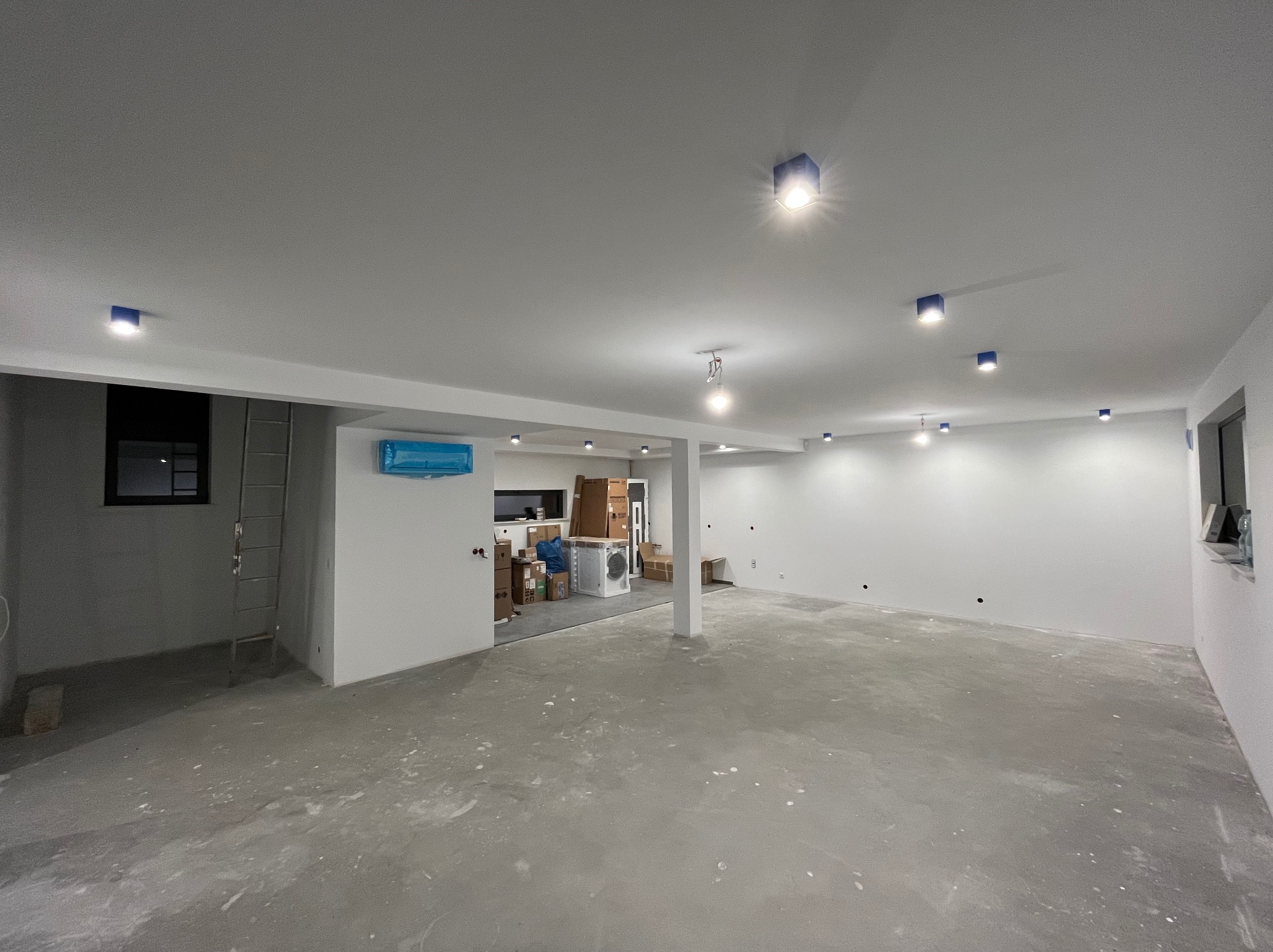 Nowoczesne, surowe wnętrze z punktowym oświetleniem LED w niebieskich obudowach. Widoczne przygotowania do wykończenia podłogi i ścian. Minimalistyczny design.