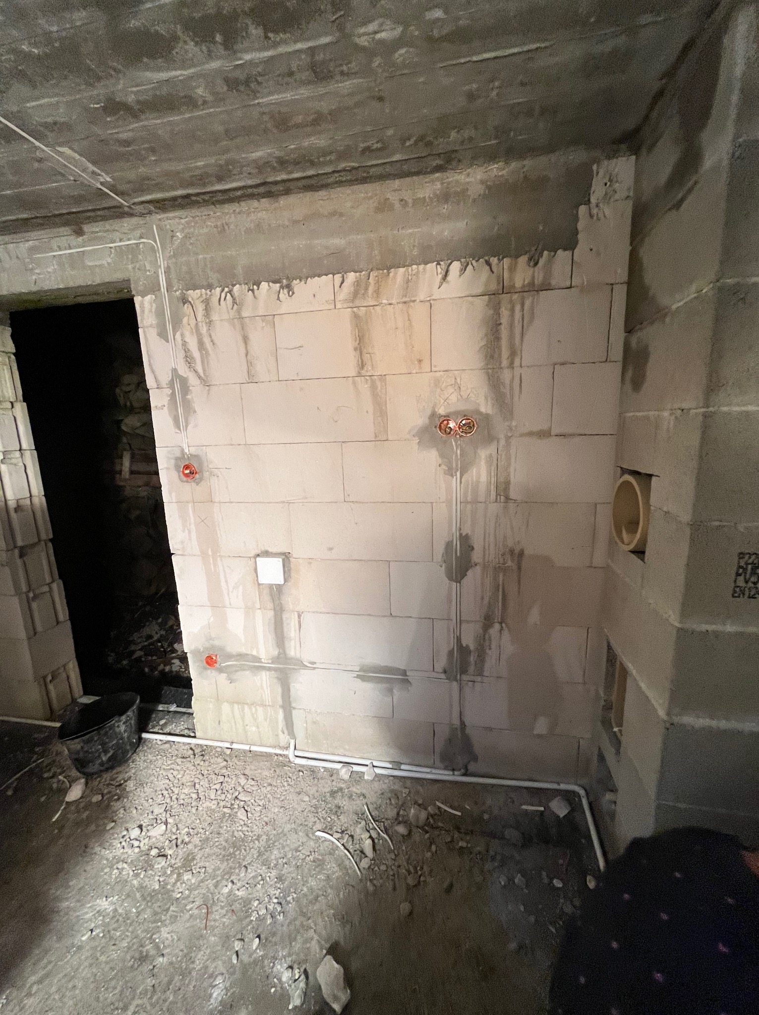 Surowy stan: instalacja elektryczna w trakcie montażu w pomieszczeniu z betonu komórkowego. Widoczne kable, puszki instalacyjne i rury. Podłoże nieutwardzone.