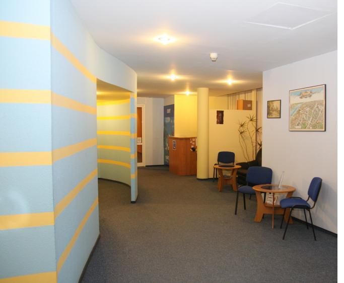 Wnętrze biura z recepcją, stolikami i krzesłami dla klientów, ściany w kolorze błękitnym z żółtymi pasami, na ścianie mapa miasta.