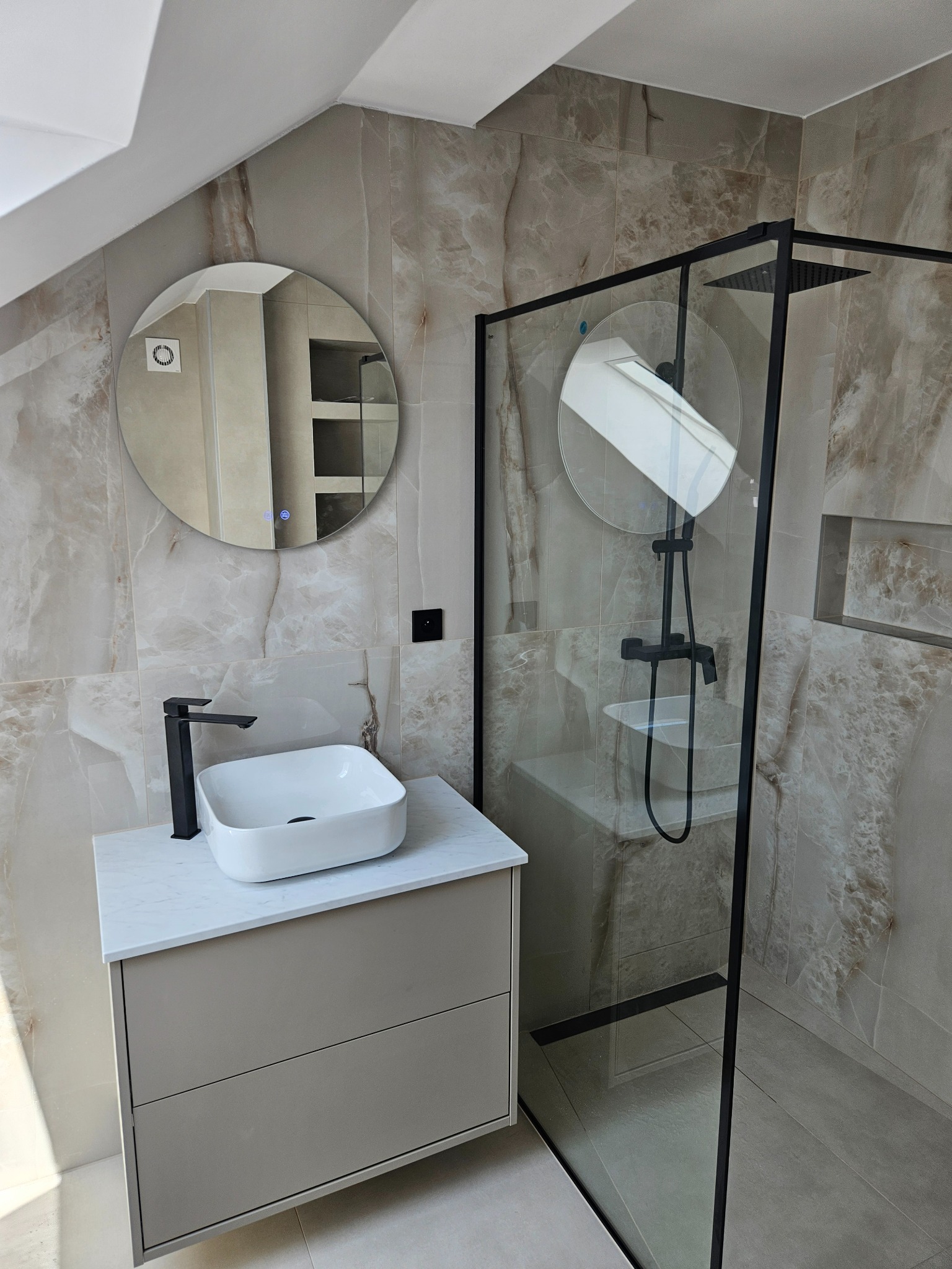 Elegancka łazienka na poddaszu z kabiną prysznicową typu walk-in, umywalką nablatową i okrągłym lustrem z podświetleniem LED. Płytki imitujące marmur w beżowych tonacjach.