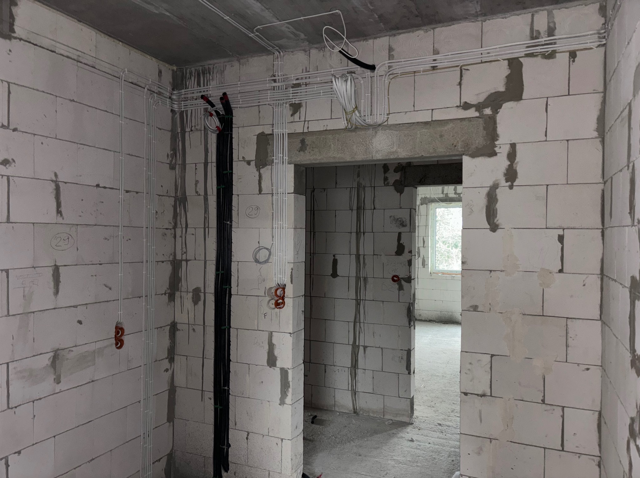 Wnętrze w stanie surowym z widoczną instalacją elektryczną: białe rurki i czarne kable prowadzone po ścianach z betonu komórkowego. Widoczne puszki instalacyjne.