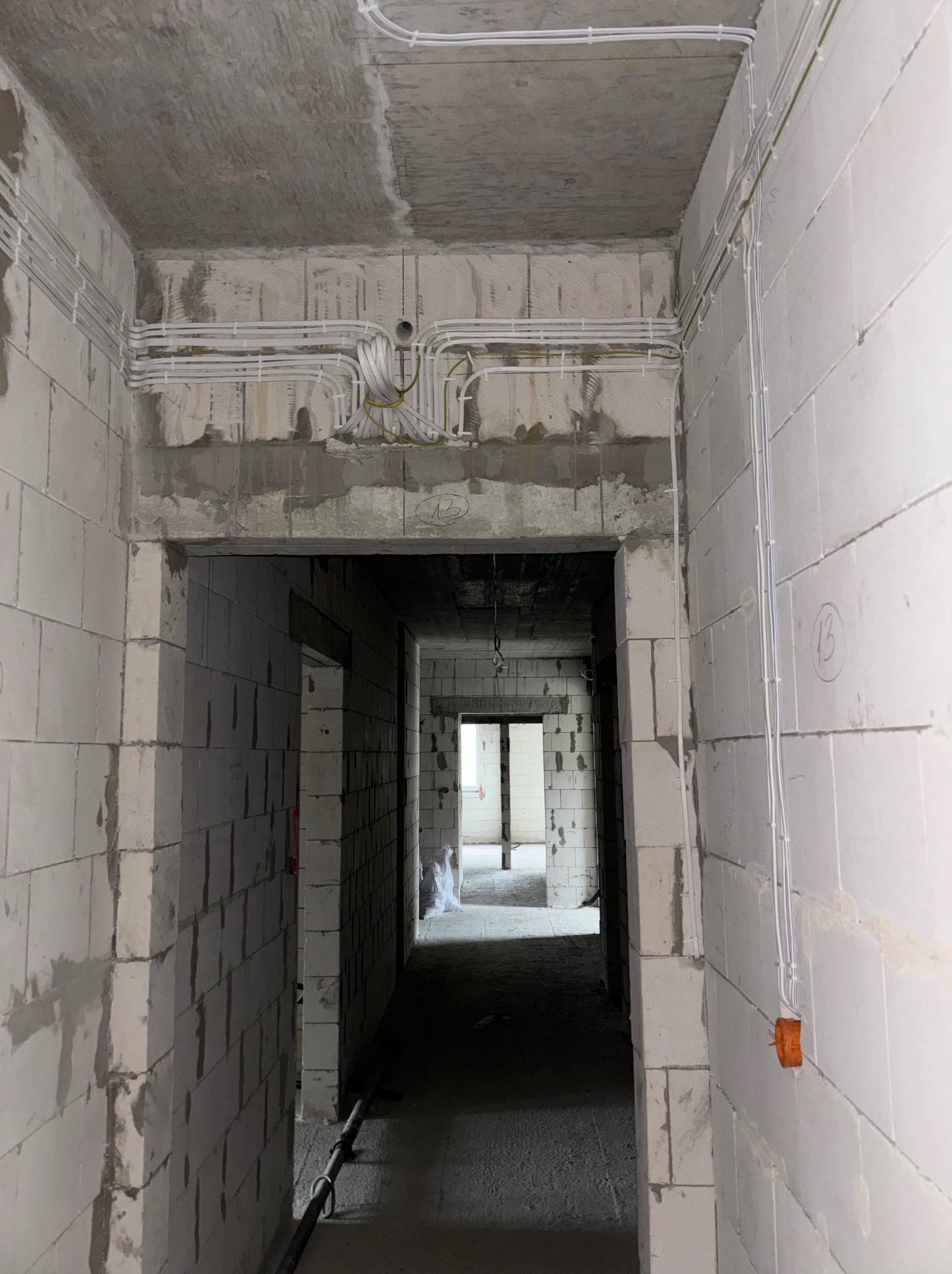 Wnętrze w stanie surowym z widoczną instalacją elektryczną: kable prowadzone po ścianach i suficie, puszki elektryczne. Widok z perspektywy korytarza.