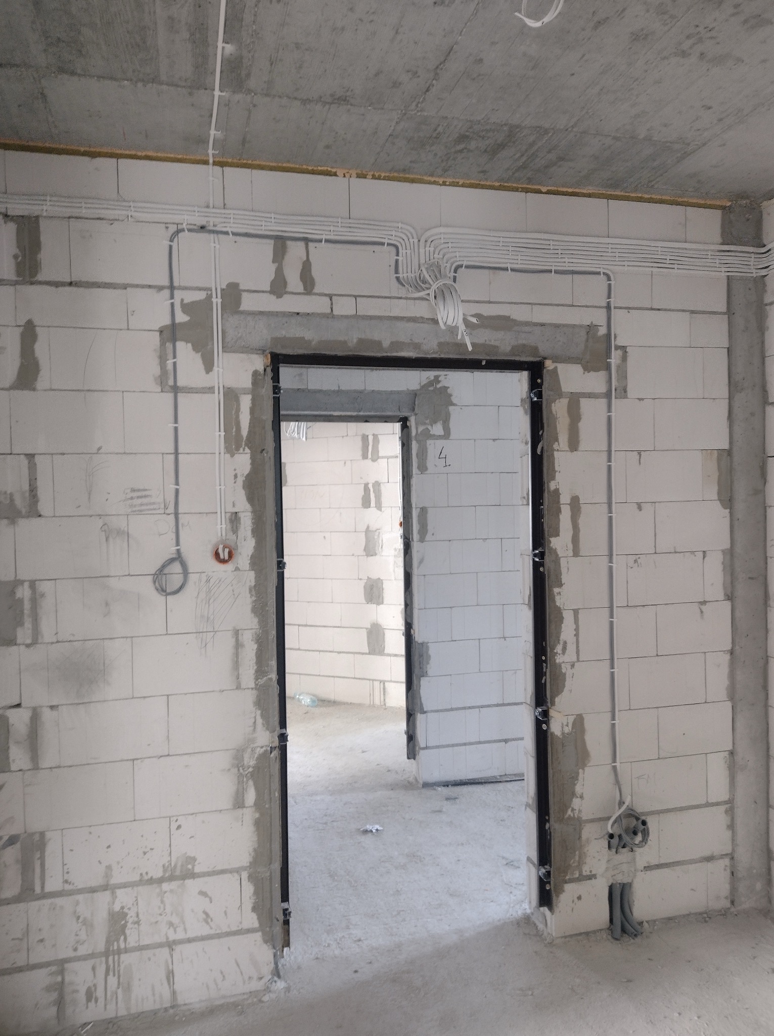 Białe kable elektryczne prowadzone po ścianach z betonu komórkowego w surowym stanie, widoczne puszki instalacyjne i otwór drzwiowy z metalową ościeżnicą.