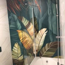 StemBau - Nowoczesna łazienka z wanną i szklanym parawanem, ściana z motywem tropikalnych liści. Biała ceramika i armatura. Minimalistyczny styl.