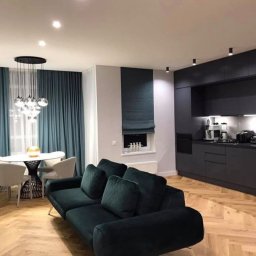 StemBau - Nowoczesne wnętrze: ciemna zabudowa kuchenna, parkiet w jodełkę, turkusowe zasłony i sofa. Minimalistyczny design z lampami punktowymi i wiszącą nad stołem.