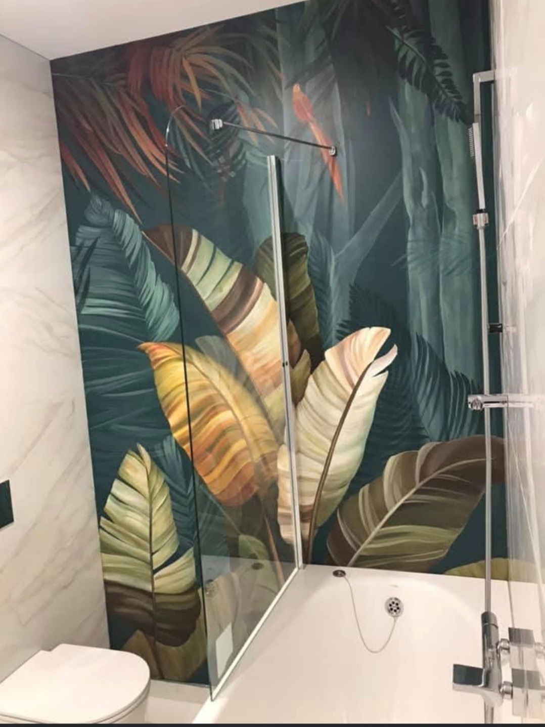 Nowoczesna łazienka z wanną i szklanym parawanem, ściana z motywem tropikalnych liści. Biała ceramika i armatura. Minimalistyczny styl.