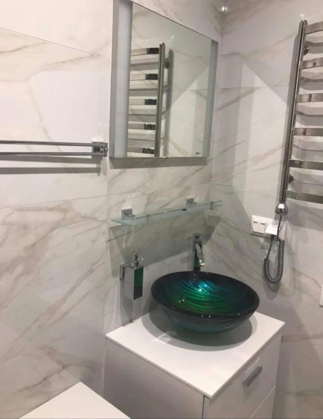 Wykończona łazienka z umywalką w odcieniach zieleni i bieli, marmurowe płytki, grzejnik drabinkowy i lustro z oświetleniem. Nowoczesny design.