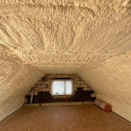 DASKO - Poddasze po ociepleniu pianą PUR, widoczne nierównomierne pokrycie pianą na skośnym dachu i ścianach, okno w szczycie, podłoga z płyt OSB.