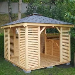 Jan Sobczyk - Drewniana altana z ażurowymi ścianami, kryta ciemnym gontem, na tle zieleni ogrodu. Widoczne betonowe bloczki fundamentowe i starannie wykonane detale konstrukcyjne.