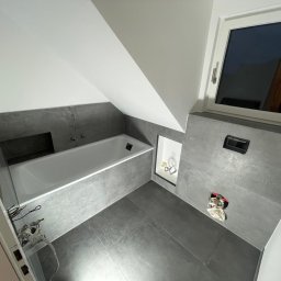 Bastix - Szara łazienka na poddaszu w Mielcu z wanną, oknem i zabudową WC. Widoczne płytki imitujące beton i biała armatura. Minimalistyczny design.
