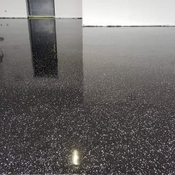 Bastix - Błyszcząca, czarna posadzka żywiczna z białymi drobinkami, odbijająca światło. Widoczne białe ściany i fragment drzwi w tle. Minimalistyczny design.