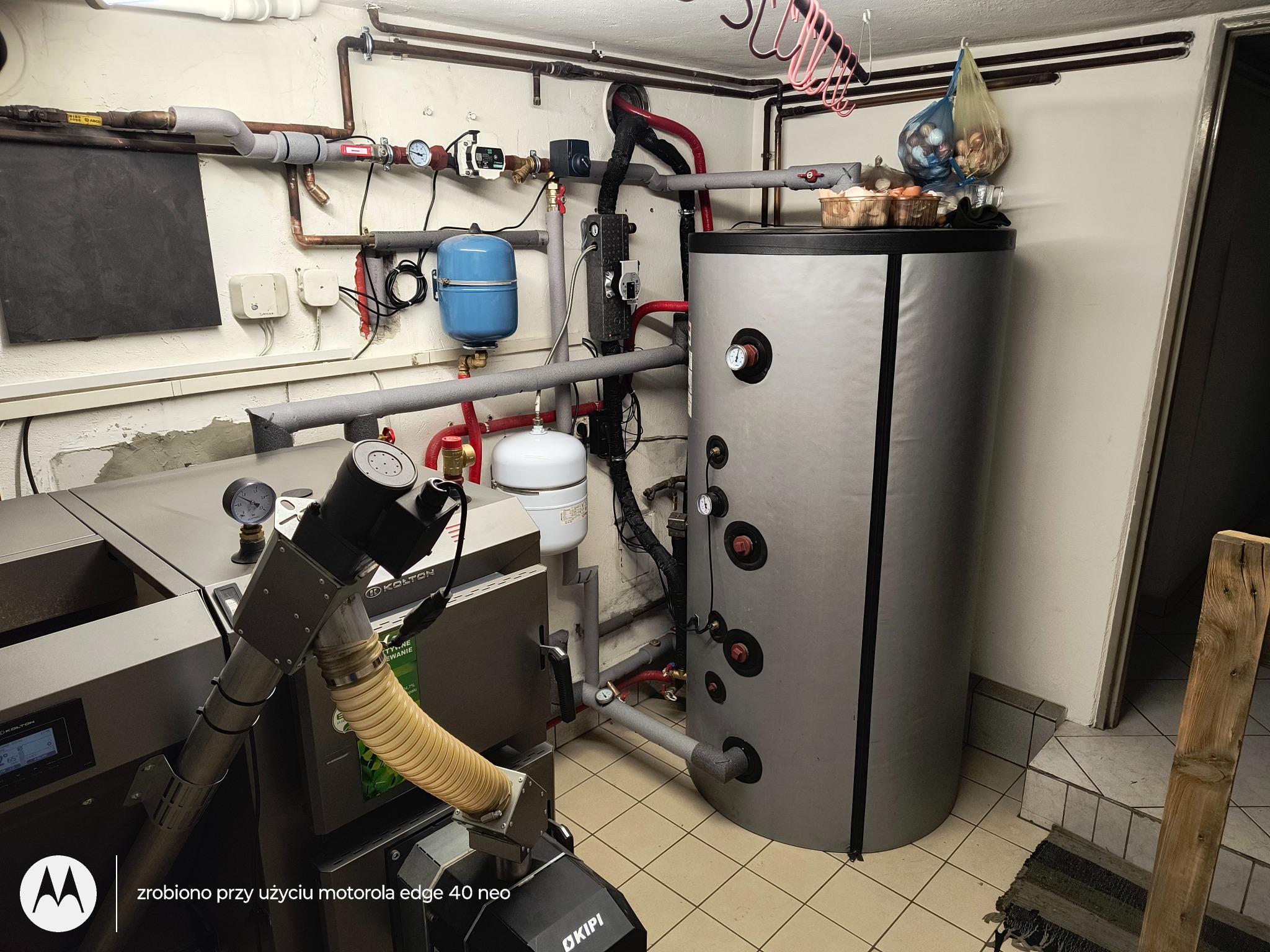 Kotłownia po modernizacji: kocioł na pellet, instalacja solarna do ciepłej wody i wsparcia CO. Widoczne rury, zbiornik akumulacyjny i elementy instalacji.