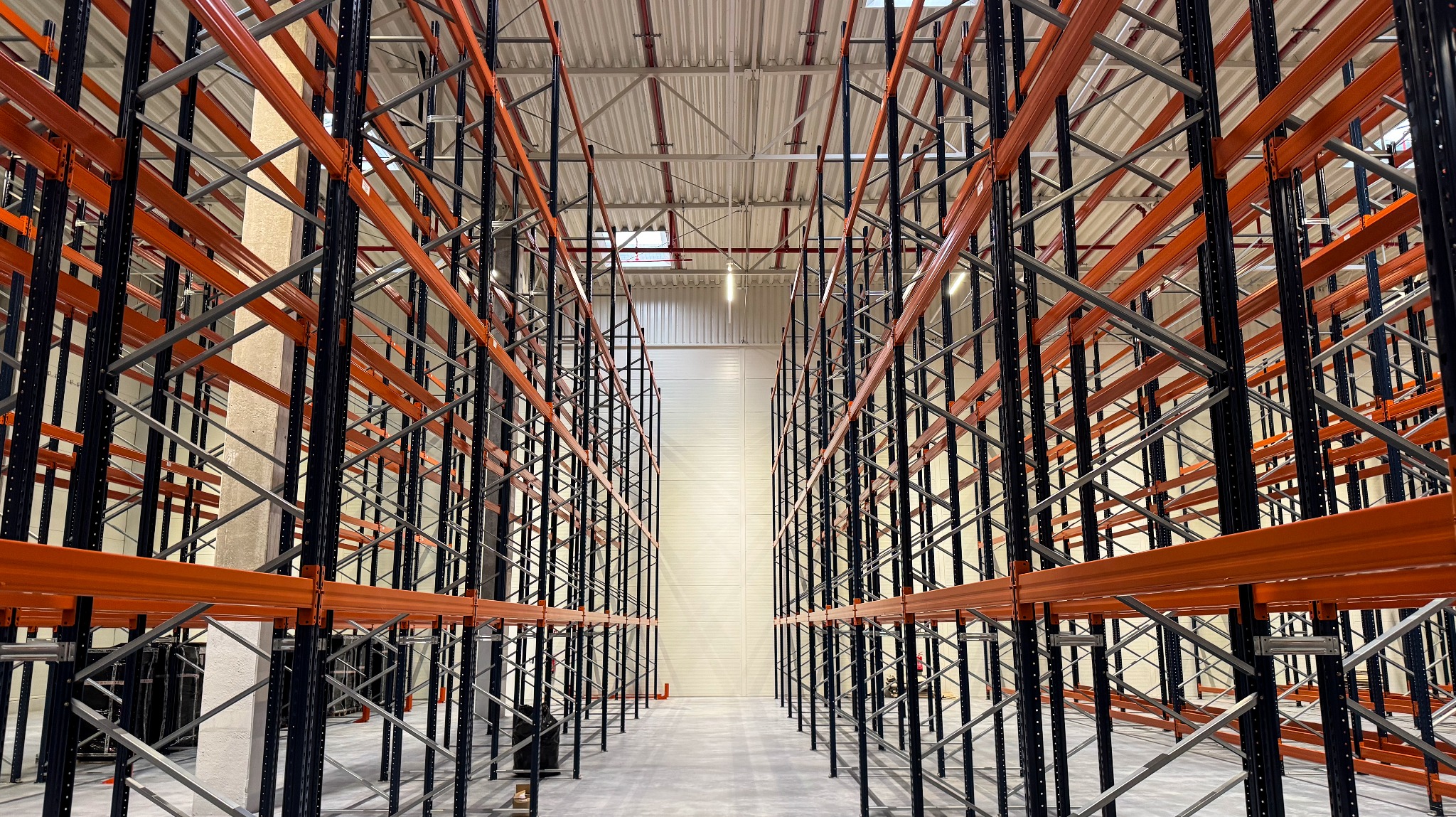Puste, pomarańczowo-czarne regały magazynowe w hali, widok z perspektywy podłogi, symetryczny układ, oświetlenie sufitowe.