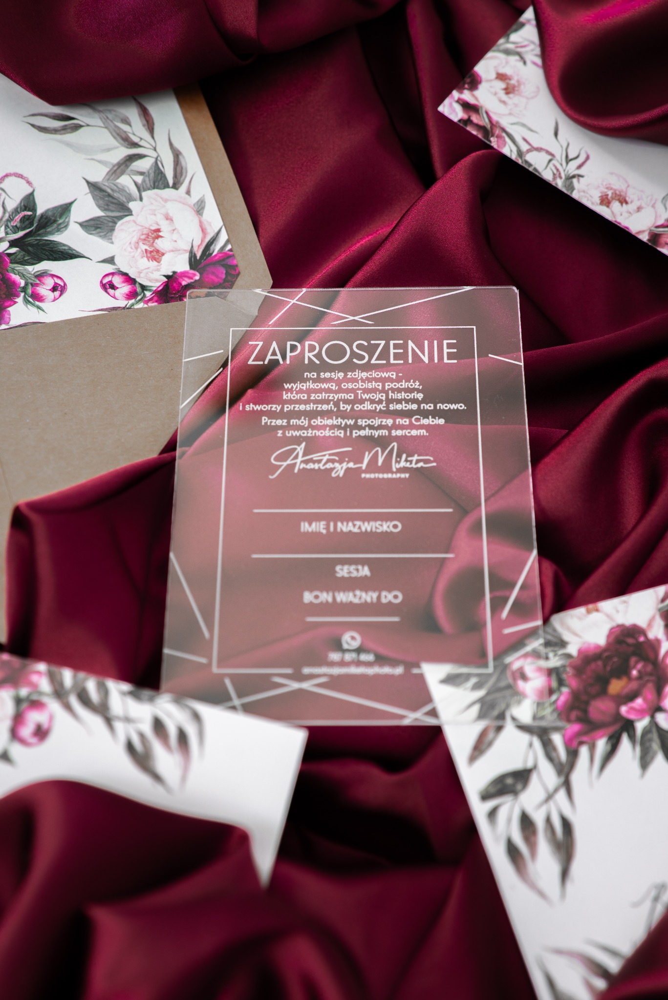 Zaproszenie na sesję zdjęciową z motywem kwiatowym na burgundowym tle. Przezroczysta karta z tekstem i danymi kontaktowymi fotografa.