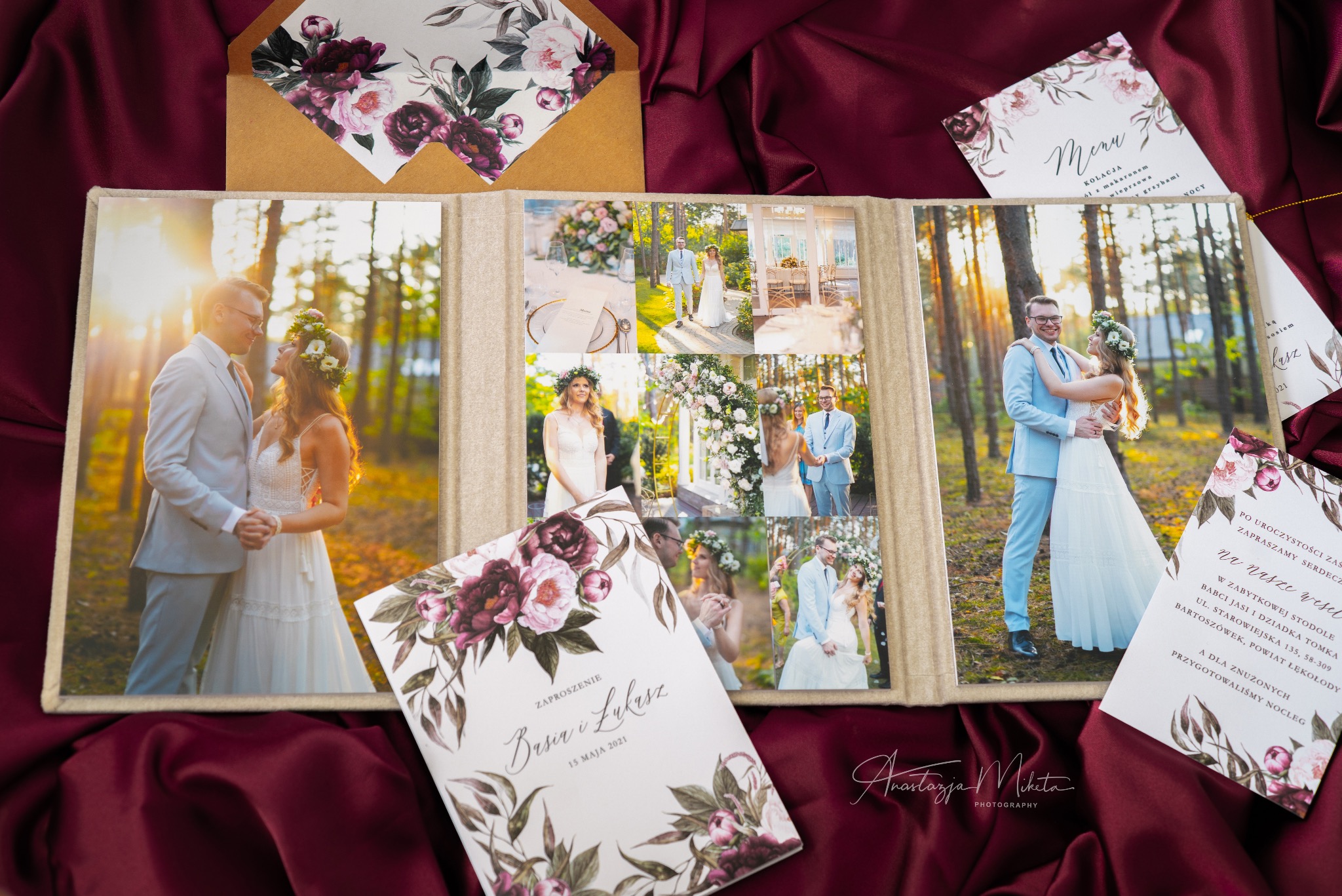 Album ślubny z kolażem zdjęć pary młodej w plenerze i zaproszenia ślubne z motywem kwiatowym na bordowej tkaninie. Widoczne detale sukni i garnituru.