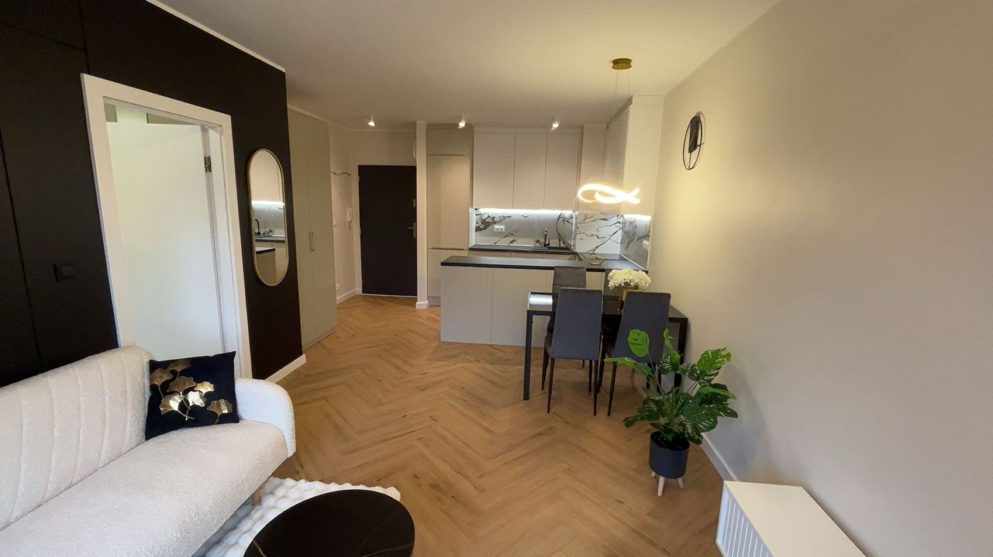 Nowoczesne wnętrze mieszkania po remoncie: parkiet w jodełkę, czarno-biała kolorystyka, minimalistyczna kuchnia z marmurowym blatem i designerskim oświetleniem.