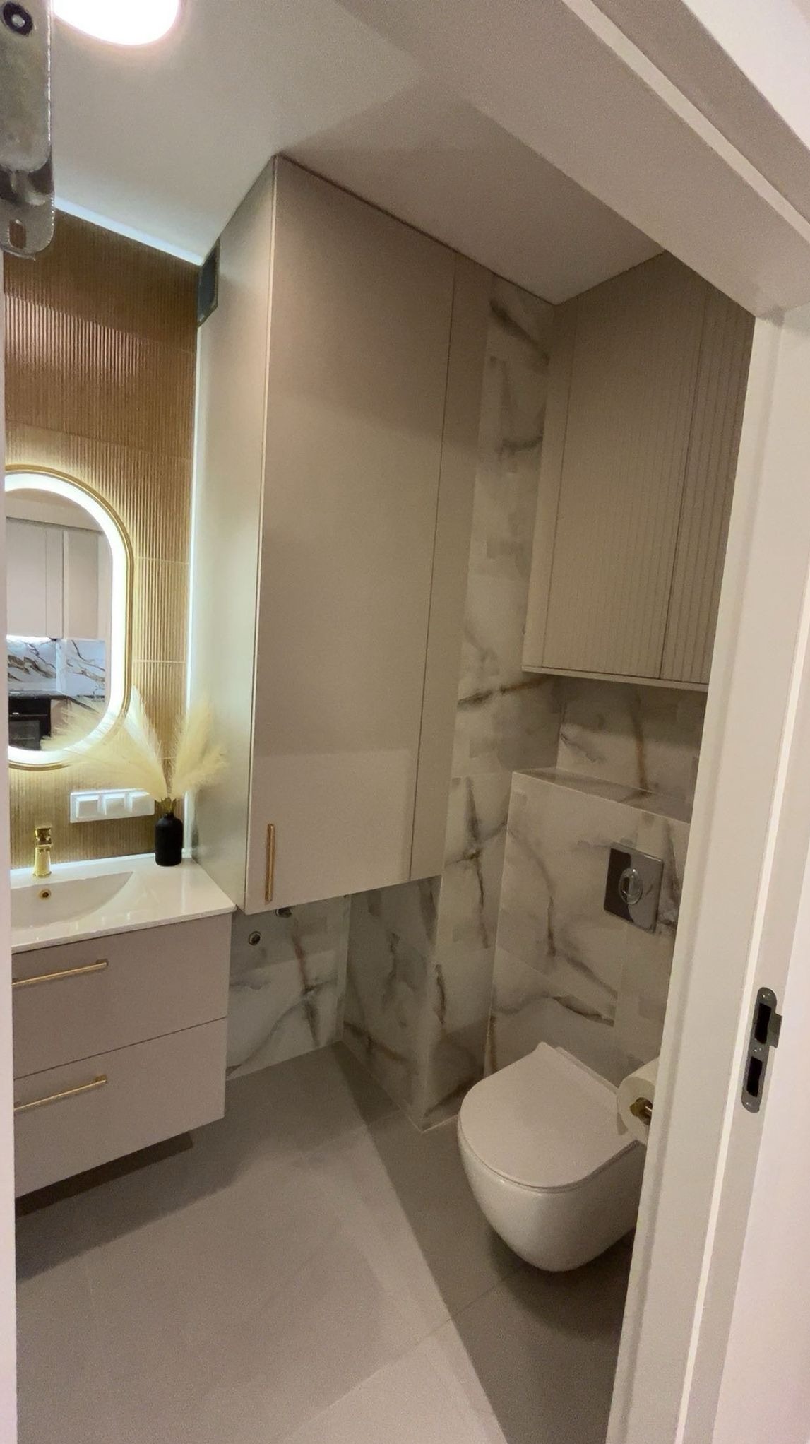 Nowoczesna łazienka w beżach z marmurowymi akcentami. Umywalka z szafką, podświetlane lustro, toaleta i szafki wiszące tworzą spójną całość.