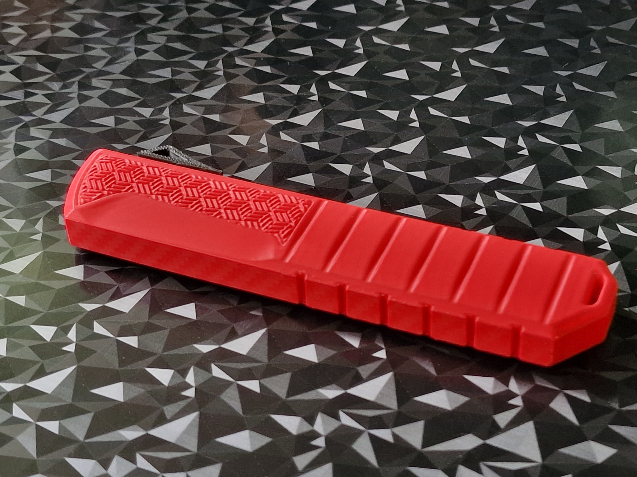 Czerwony, prostokątny element z tworzywa sztucznego z geometrycznym wzorem na tle czarno-białej, trójkątnej mozaiki. Widoczna faktura materiału.