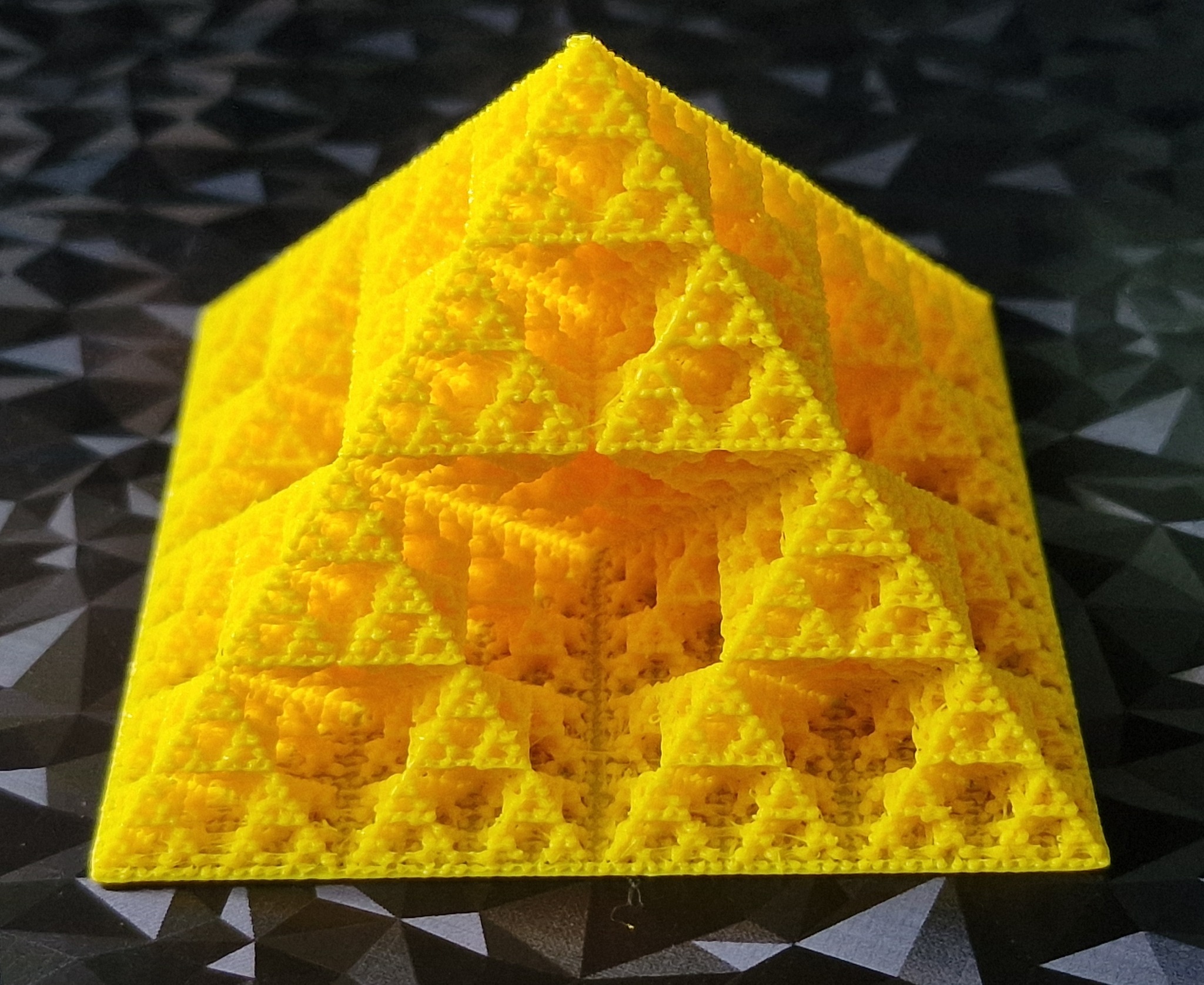 Żółta piramida Sierpińskiego, model matematyczny z precyzyjnymi detalami, na tle geometrycznym. Ukazanie możliwości dokładnego odwzorowania skomplikowanych struktur.