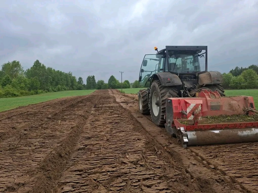 Ciężki traktor z mulczerem na polu, świeżo po frezowaniu pni i korzeni. Przygotowanie terenu pod uprawę, widok z boku na maszynę i obrobioną glebę.