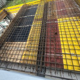 Zbrojenie stropu na deskowaniu z żółtymi i czerwonymi elementami, widok z góry. Metalowa siatka z prętów, przygotowanie do wylewania betonu.