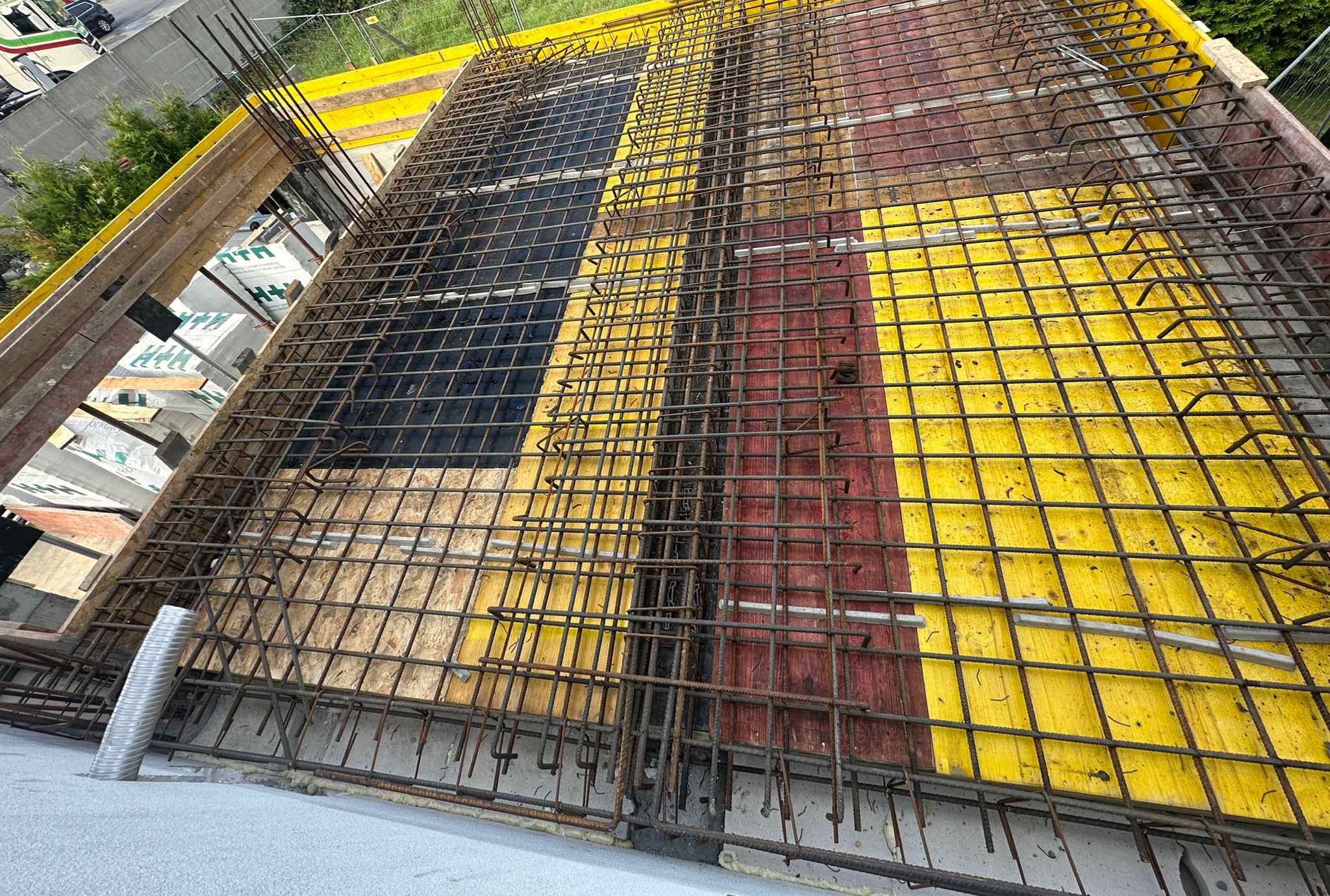 Zbrojenie stropu na deskowaniu z żółtymi i czerwonymi elementami, widok z góry. Metalowa siatka z prętów, przygotowanie do wylewania betonu.