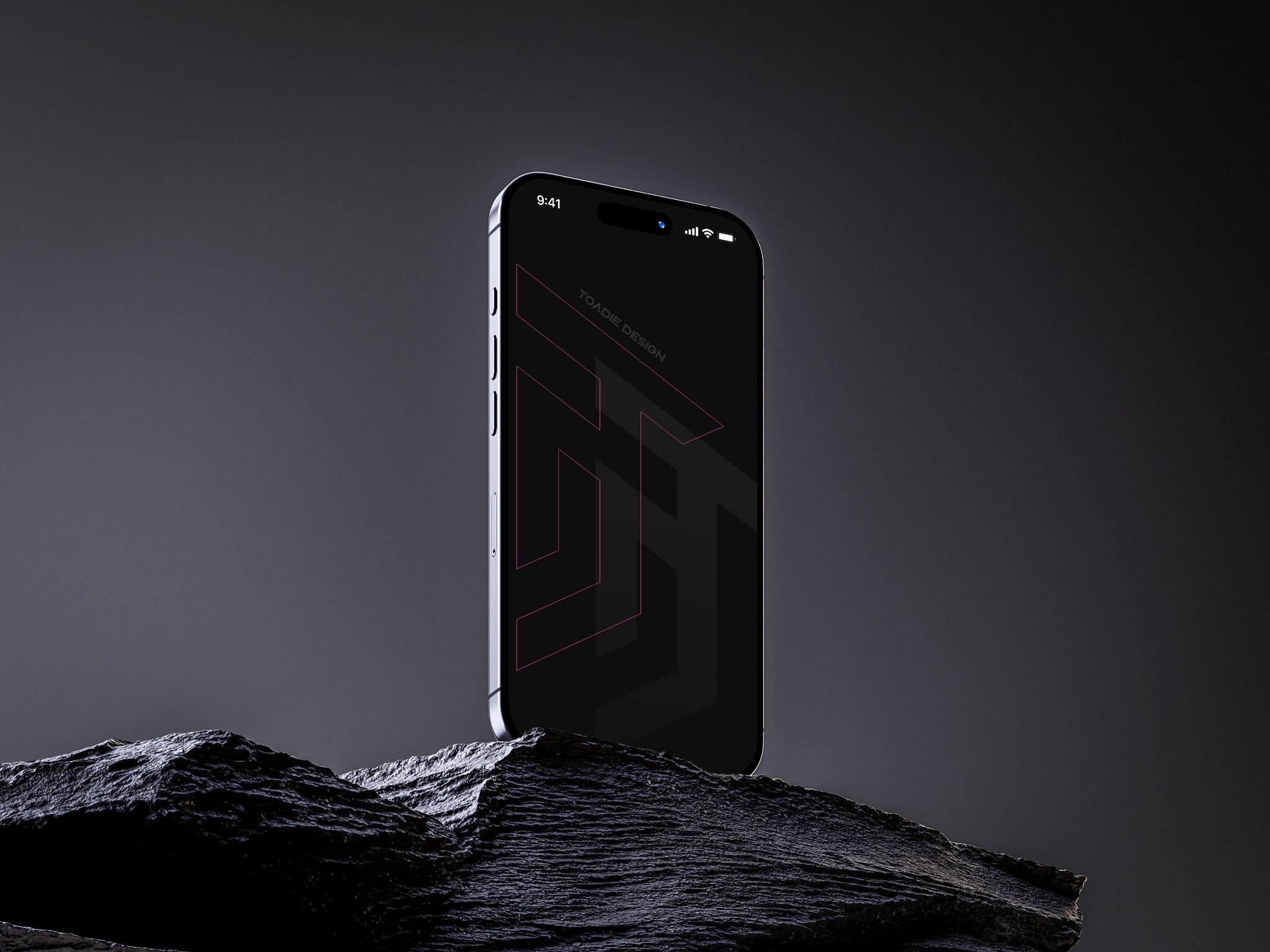 Smartfon z logo 'Toadie Design' na ekranie, ustawiony na ciemnej, teksturowanej skale. Minimalistyczny design, stonowana kolorystyka, profesjonalna prezentacja.
