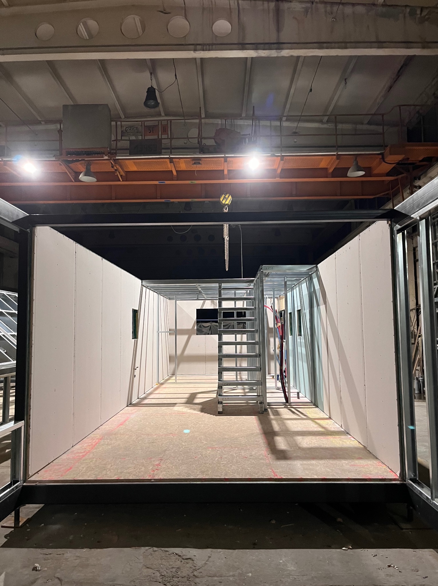 Wnętrze modułowej konstrukcji z płyt karton-gips na metalowym stelażu, widok z zewnątrz, surowy stan wykończenia, widoczne instalacje i schody.