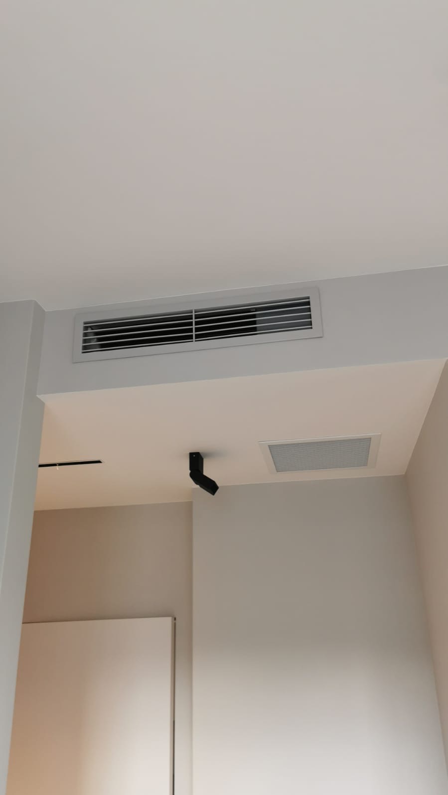 Nowoczesny system wentylacyjny z kratką w suficie, uzupełniony o punktowe oświetlenie. Minimalistyczny design w jasnych barwach.