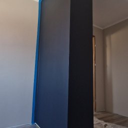 Łukasz Hanas - Świeżo pomalowany filar w kolorze granatowym, zabezpieczony taśmą malarską i folią ochronną na podłodze w Michałowie. Widoczne detale wykończenia.