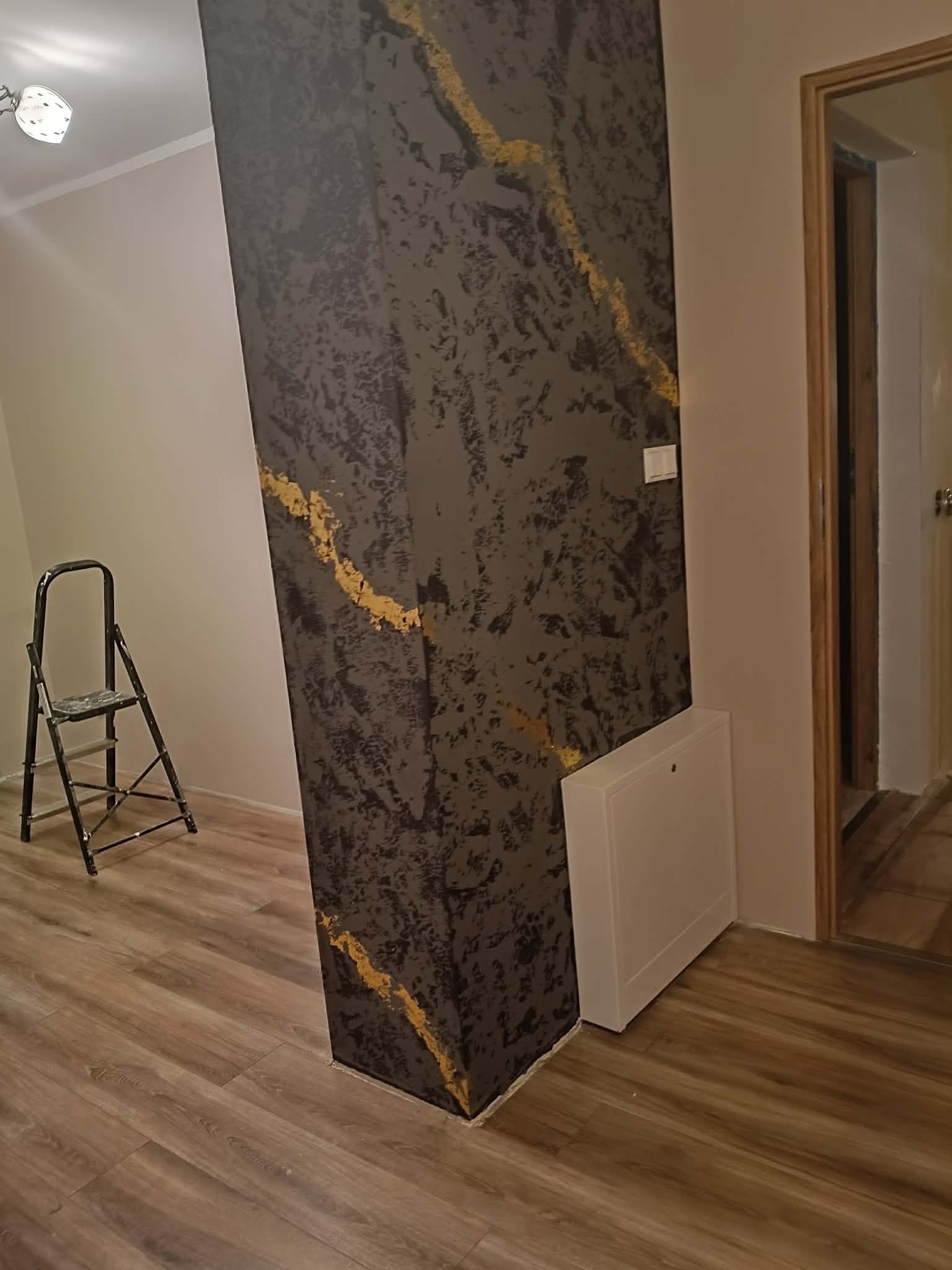 Dekoracyjna kolumna w pokoju z efektem marmuru i złotymi żyłkami, drabina malarska w tle. Wykończenie wnętrza z dbałością o detale.