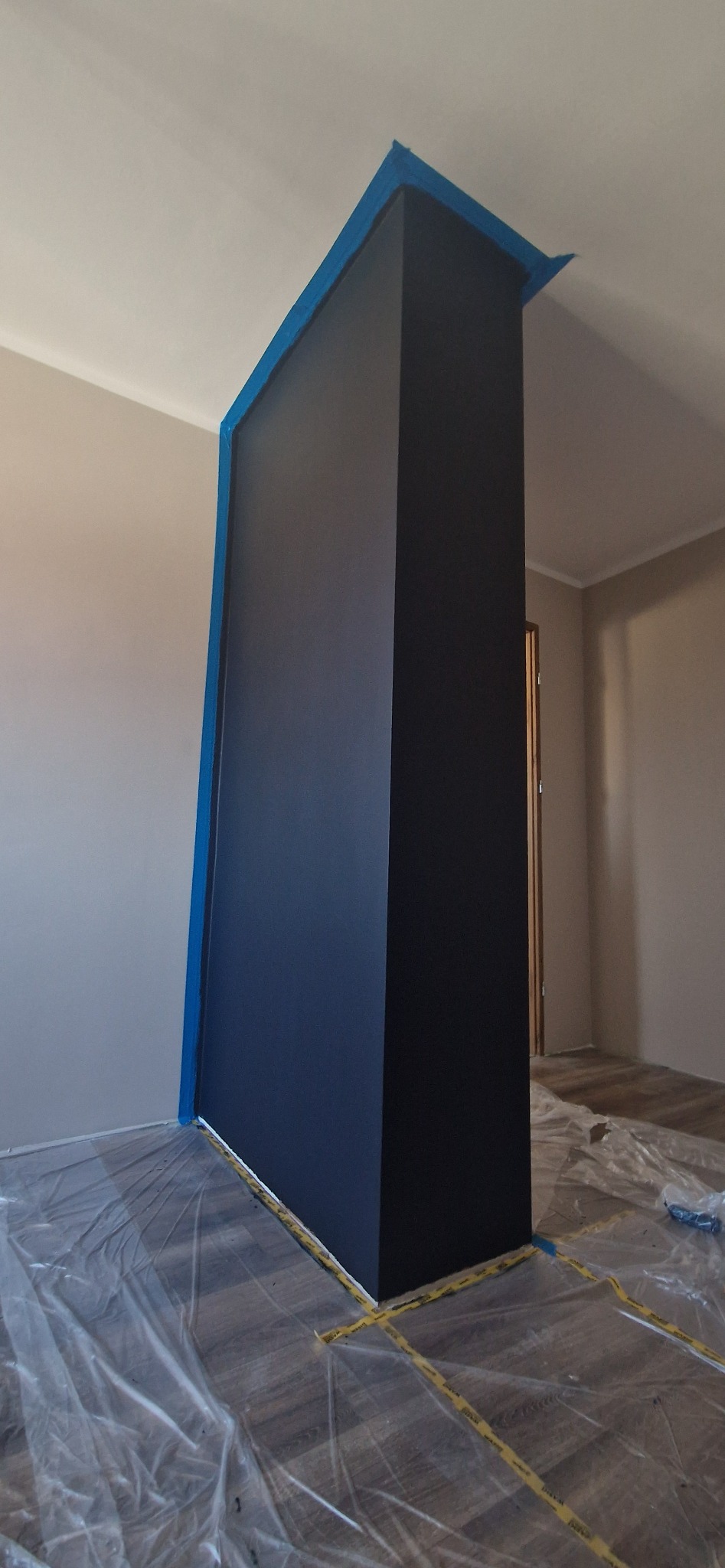 Świeżo pomalowany filar w kolorze granatowym, zabezpieczony taśmą malarską i folią ochronną na podłodze w Michałowie. Widoczne detale wykończenia.