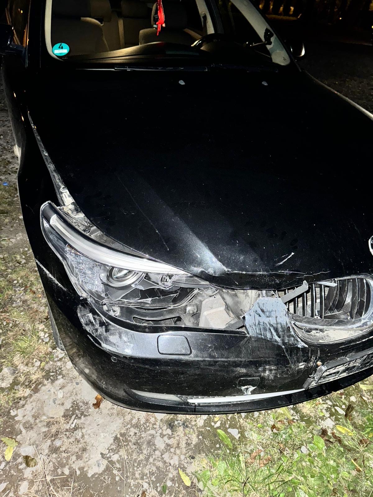 Uszkodzony przód czarnego BMW E60: pęknięta lampa, zarysowany zderzak, uszkodzona maska. Widoczne ślady kolizji i zniszczenia elementów karoserii.