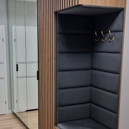 Nowoczesna zabudowa przedpokoju z siedziskiem tapicerowanym, wnęką na wieszaki i lustrem. Drewniane lamele tworzą ażurową ściankę. Minimalistyczny design.