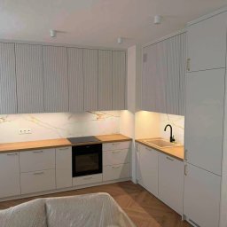 PIJAR Daniel Przesmycki - Jasna kuchnia z drewnianym blatem i marmurowym panelem. Górne szafki z ryflowanymi frontami. Nowoczesny design z oświetleniem LED podszafkowym.