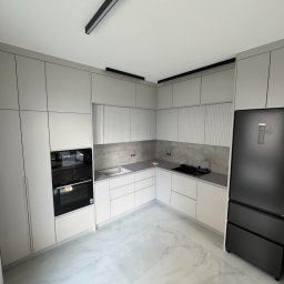 PIJAR Daniel Przesmycki - Jasna kuchnia z szarymi frontami, czarnym sprzętem AGD i oświetleniem szynowym. Minimalistyczny design, marmurowa podłoga, widok na całe pomieszczenie.