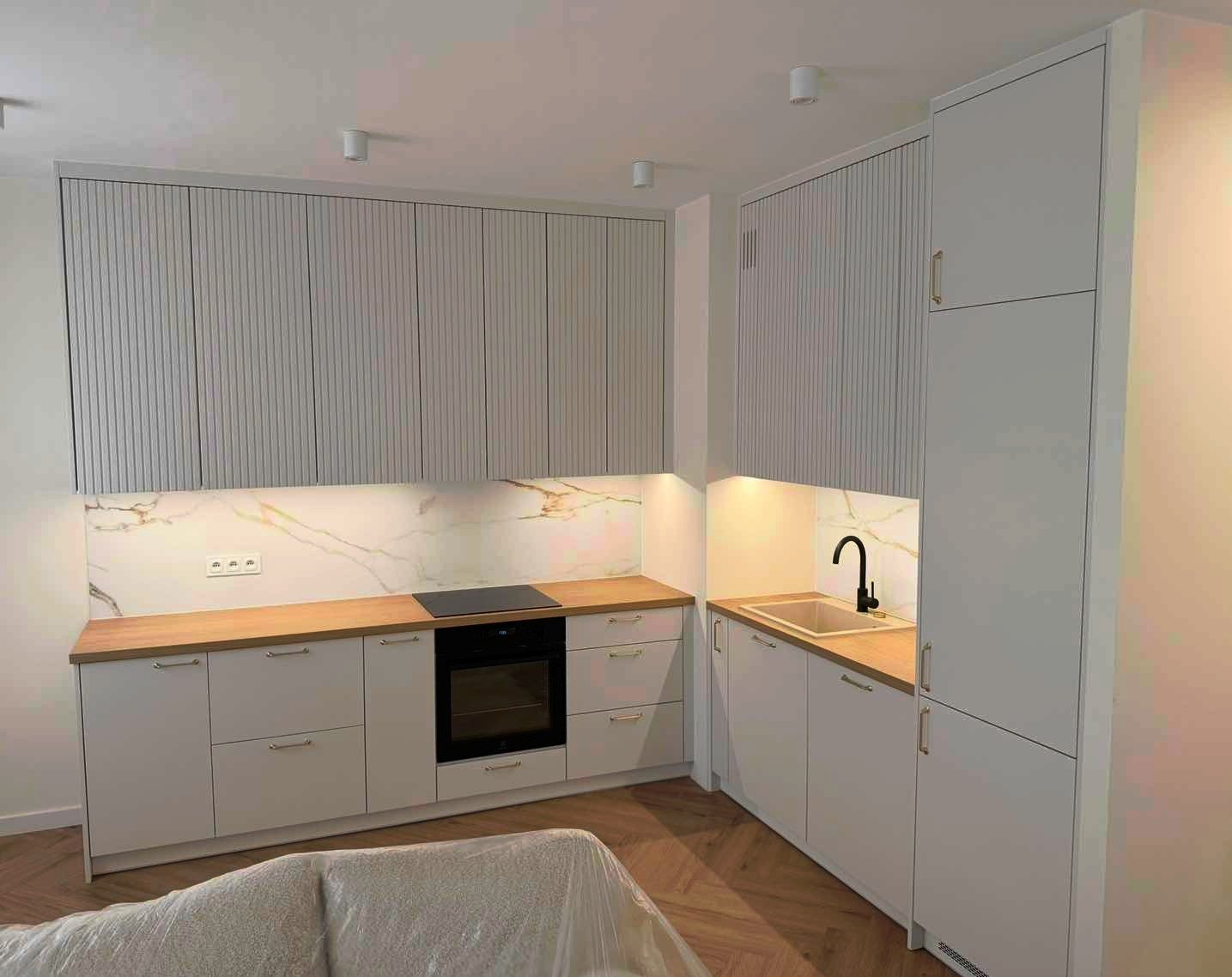 Jasna kuchnia z drewnianym blatem i marmurowym panelem. Górne szafki z ryflowanymi frontami. Nowoczesny design z oświetleniem LED podszafkowym.