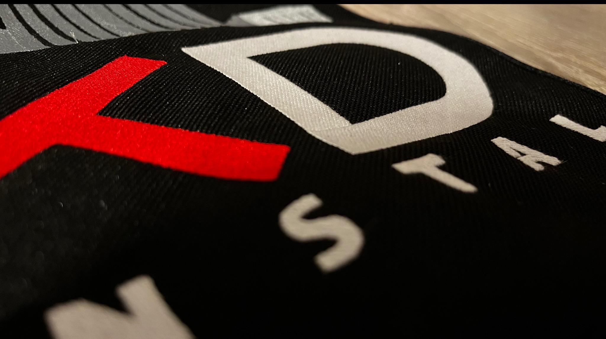 Czarno-biała tkanina z czerwonym akcentem, na której widnieje napis 'INSTAL'. Ujęcie z bliska, ukazujące detale materiału i precyzję wykonania nadruku.