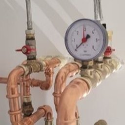 NIEZALEŻNY DOM SPÓŁKA Z OGRANICZONĄ ODPOWIEDZIALNOŚCIĄ - Instalacja hydrauliczna z miedzianymi rurami, manometrem i zaworami, zamontowana na białej ścianie. Widoczna pompa obiegowa. Ujęcie z bliska.