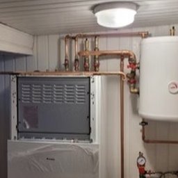 NIEZALEŻNY DOM SPÓŁKA Z OGRANICZONĄ ODPOWIEDZIALNOŚCIĄ - Biały, częściowo ofoliowany piec z miedzianą instalacją grzewczą w pomieszczeniu wykończonym panelami ściennymi i sufitowych. Widoczny zbiornik i manometr.