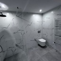 KrissGlaz - Nowoczesna łazienka z marmurowymi płytkami, kabiną prysznicową typu walk-in, podwieszaną toaletą i grzejnikiem drabinkowym. Minimalistyczny design, szaro-biała kolorystyka.