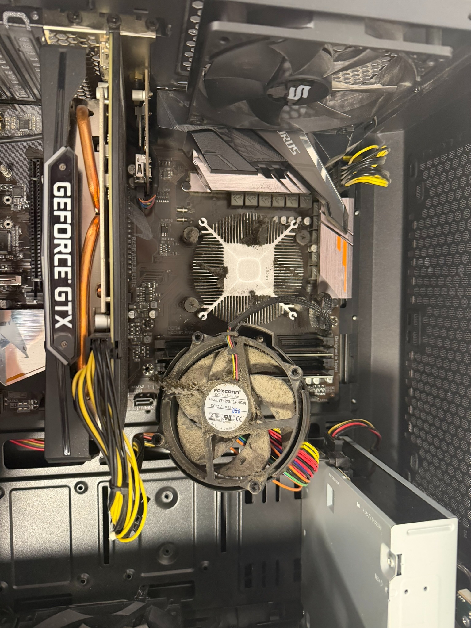 Wnętrze obudowy komputera stacjonarnego z zakurzoną kartą graficzną GeForce GTX, płytą główną Aorus Elite i wentylatorem Foxconn. Widoczne kable i radiator.