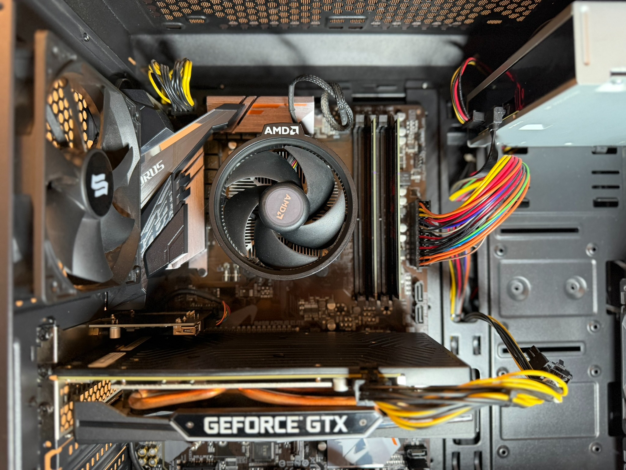 Wnętrze komputera stacjonarnego z widoczną kartą graficzną GeForce GTX, procesorem AMD z chłodzeniem i kolorowymi kablami zasilającymi. Widok z góry.